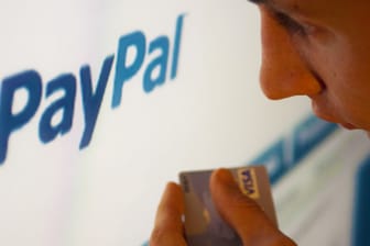 Mann hält Bankkarte in der Hand und schaut auf Paypal-Konto
