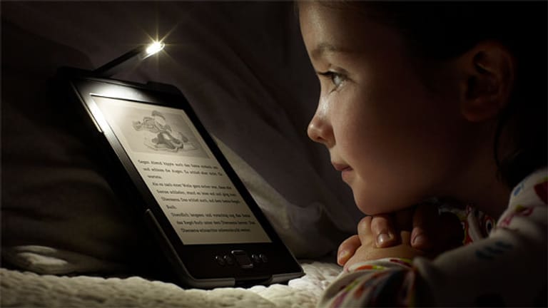 Kind liest im Bett mit einem E-Book-Reader von Amazon.
