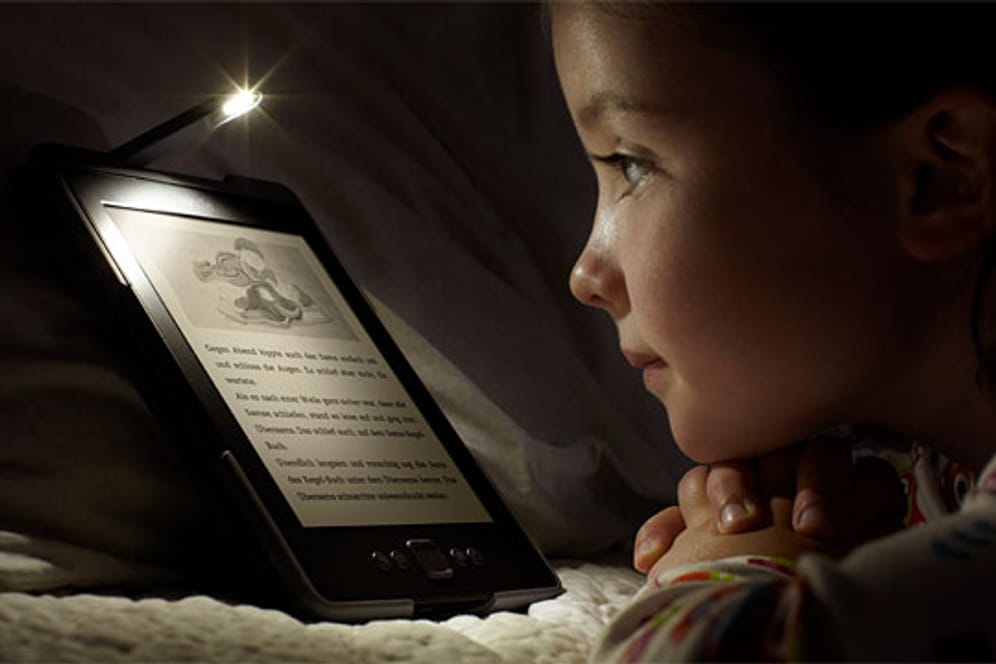 Kind liest im Bett mit einem E-Book-Reader von Amazon.
