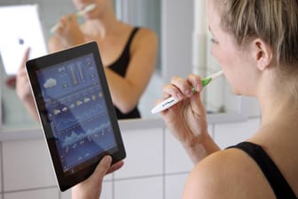 Eine junge Frau schaut beim Zähneputzen auf einem iPad nach der Wettervorhersage.
