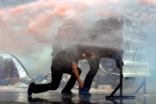 Demonstranten kauern hinter einer Barrikade, um sich vor einem Wasserwerfer zu schützen
