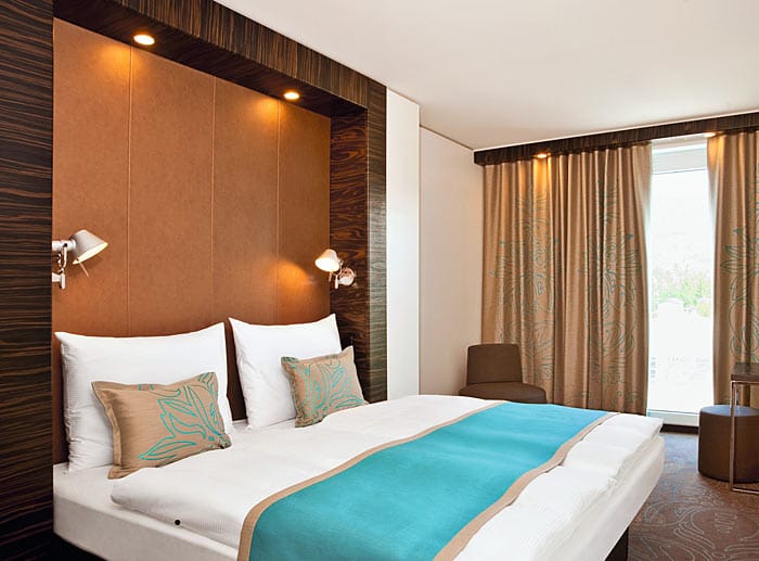 In den Zimmern sorgen türkise Ornamente auf Teppichboden, Vorhänge und Kissen für farbige Akzente. Hotel buchbar ab 77 Euro pro Person und Nacht.