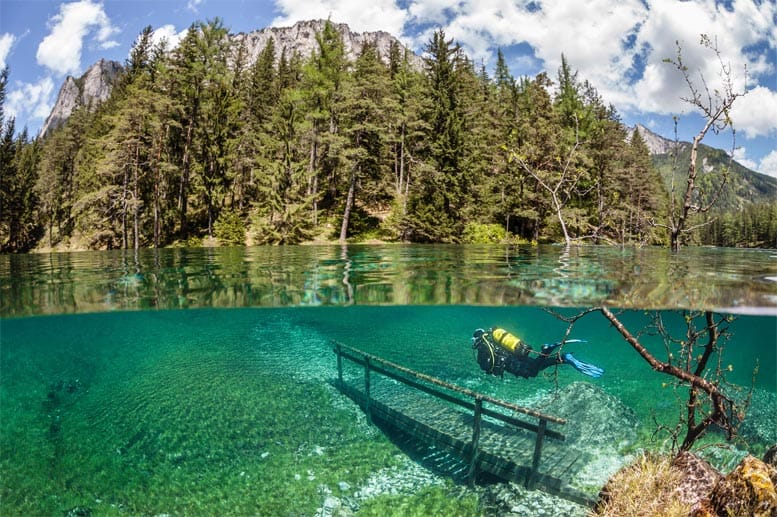Wo sonst Spaziergänger im österreichischen Tragössertal den Blick auf die Berge genießen, schwimmt ein Taucher über einen Steg im Grünen See.