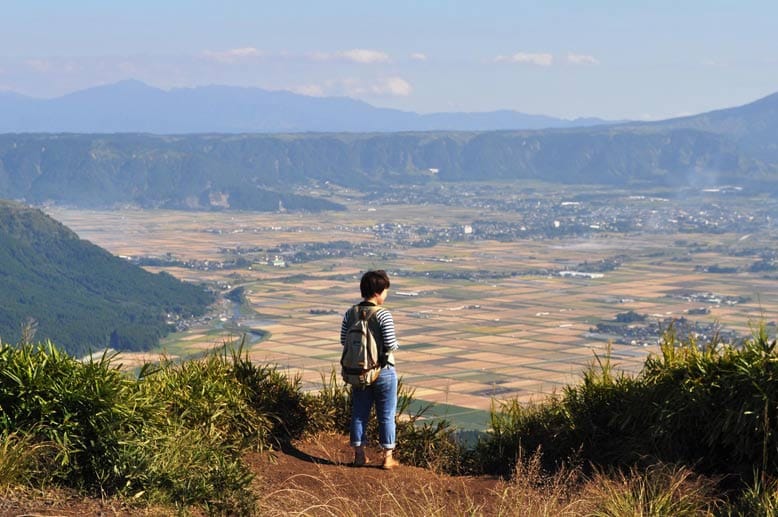 Der Aussichtspunkt Kuju Aso Nationalpark: Die Grasebene am Fuß des 1500 Meter hohen Aso-Vulkans, schimmert samtig in der Sonne. Manche Bauern mähen dort noch mit der Sense, am Straßenrand stehen kleine Jisu-Figuren zum Schutz der Reisenden. Die Schneisen ringsum des Talkessels zeigen noch immer den Weg, den einst die Lava genommen hat.