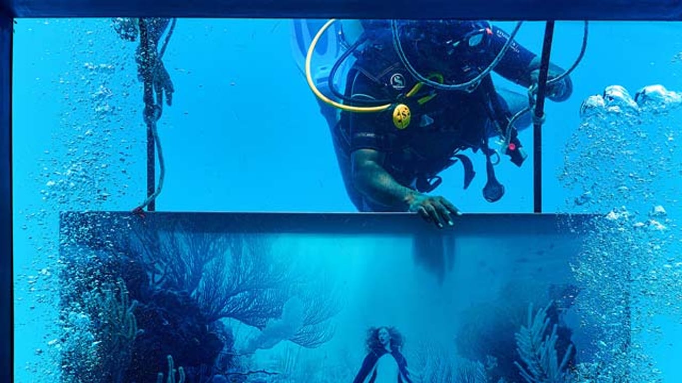 Hier befestigt ein Taucher ein Werk, welches das Märchen von Rotkäppchen zeigt, in der Unterwasser-Galerie.