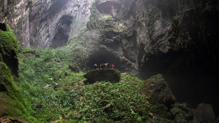 In der Son Doong ist unter einem Durchbruch im Dach der Höhle ein Dschungel gewachsen. Die Besucher erklimmen einen bewachsenen Felsen, um die Aussicht zu genießen.