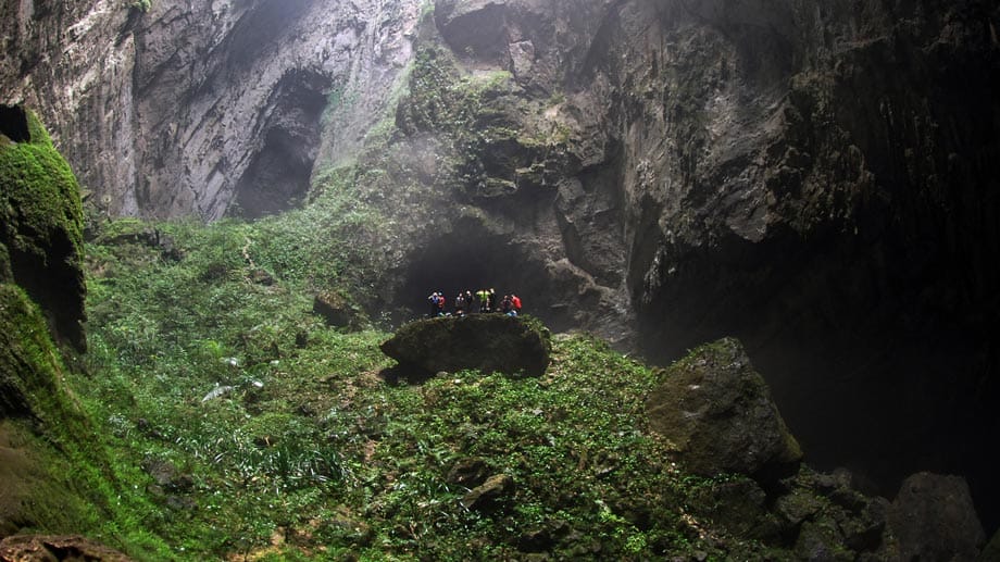 In der Son Doong ist unter einem Durchbruch im Dach der Höhle ein Dschungel gewachsen. Die Besucher erklimmen einen bewachsenen Felsen, um die Aussicht zu genießen.