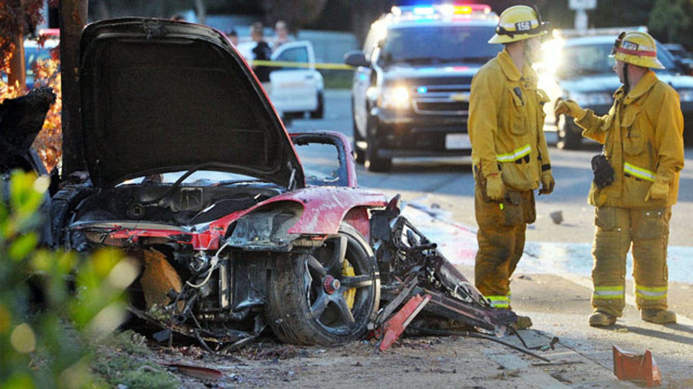 Feuerwehrmänner löschen den völlig zerstörten Sportwagen, in dem Paul Walker und Roger Rodas ums Leben kamen.