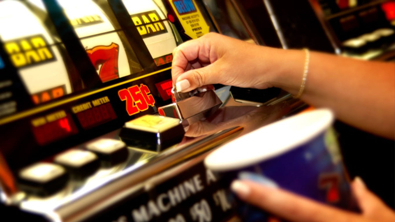 Hand wirft Münze in Spielautomat ein.