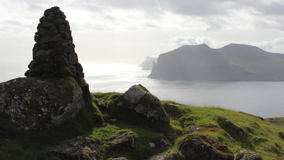Auf den Färöer Inseln tauchen Fabelwesen überall in der Natur auf: Zum Beispiel beim Trøllkonufingur, dem Hexenfinger, einem Monolith an der Südküste von Vágar (hinten).
