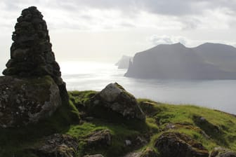 Auf den Färöer Inseln tauchen Fabelwesen überall in der Natur auf: Zum Beispiel beim Trøllkonufingur, dem Hexenfinger, einem Monolith an der Südküste von Vágar (hinten).