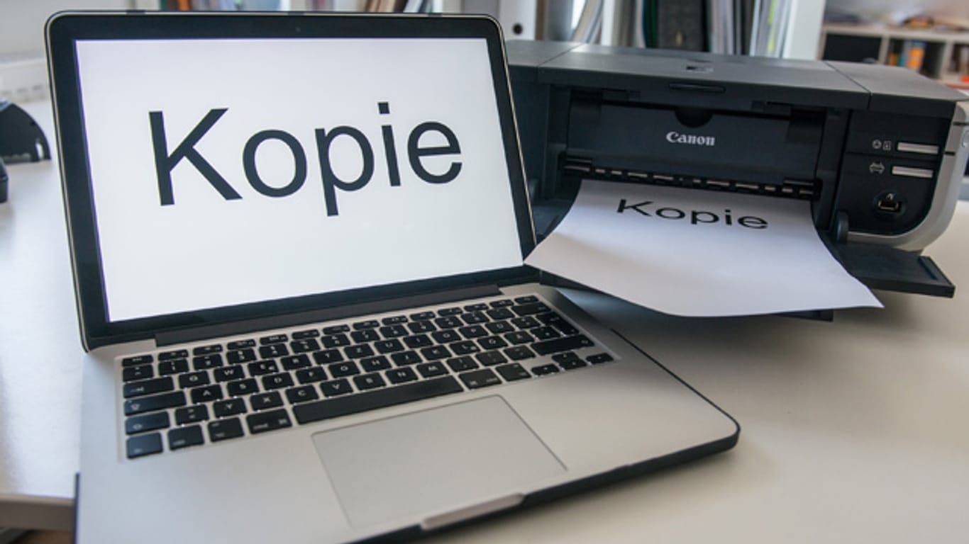 "Kopie" steht auf dem Monitor eines Laptops neben einem Drucker.