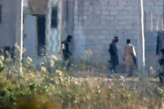 Kämpfer - vermutlich des IS - schleichen durch einen Außenbezirk von Kobane