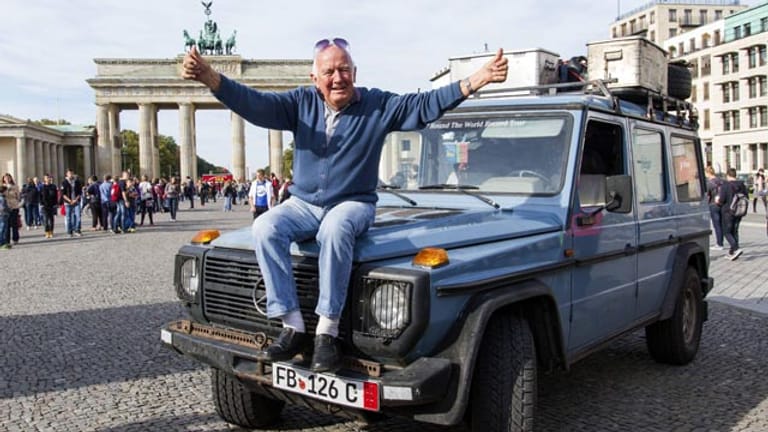 Der Weltreisende Gunther Holtorf sitzt bei seiner Ankunft in Berlin vor dem Brandenburger Tor auf der Motorhaube seines Geländewagens.
