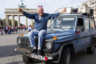 Der Weltreisende Gunther Holtorf sitzt bei seiner Ankunft in Berlin vor dem Brandenburger Tor auf der Motorhaube seines Geländewagens.
