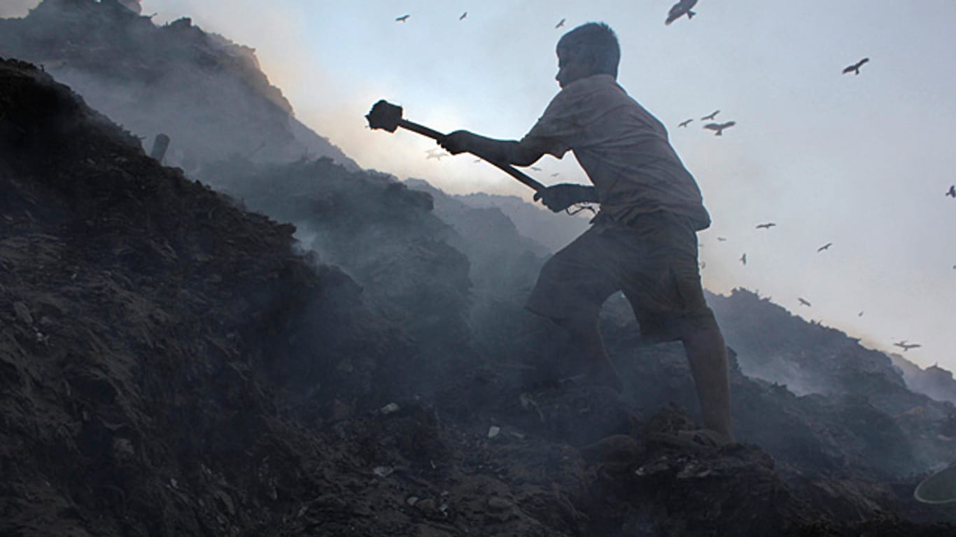 Ein elf Jahre alter Junge in Indien stochert im Müll nach Metallteilen, die er einsammeln muss