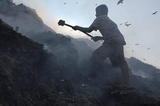 Ein elf Jahre alter Junge in Indien stochert im Müll nach Metallteilen, die er einsammeln muss