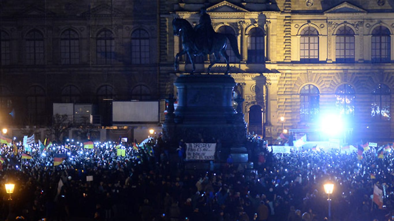 Pegida-Anhänger in Dresden, die Weihnachtslieder singen wollten, stehen im Dunkeln - die Verantwortlichen der Semperoper haben aus Protest gegen Rechts die Festbeleuchtung ausgeschaltet.