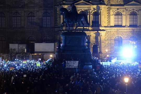 Pegida-Anhänger in Dresden, die Weihnachtslieder singen wollten, stehen im Dunkeln - die Verantwortlichen der Semperoper haben aus Protest gegen Rechts die Festbeleuchtung ausgeschaltet.