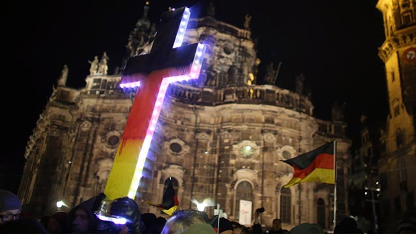 Pegida-Demonstranten halten ein Kreuz während einer Kundgebung in Dresden in den Himmel.