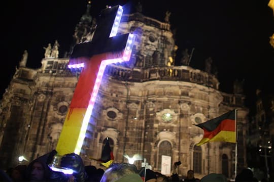 Pegida-Demonstranten halten ein Kreuz während einer Kundgebung in Dresden in den Himmel.