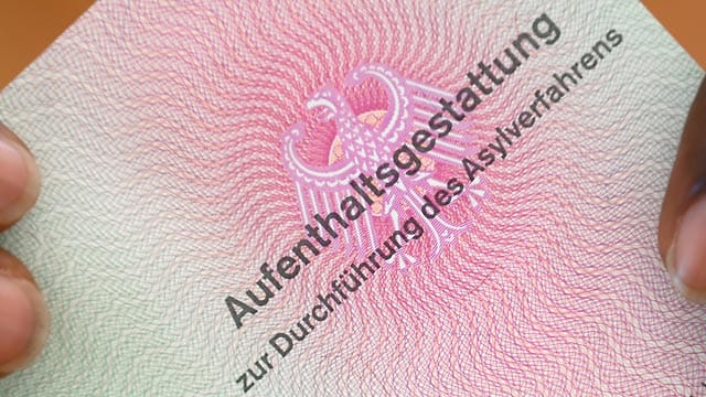 Ein Flüchtling hält eine Aufenthaltsgestattung in den Händen.