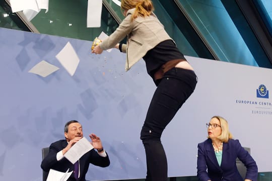 Eine Aktivistin springt vor EZB-Präsident Mario Draghi auf den Tisch.