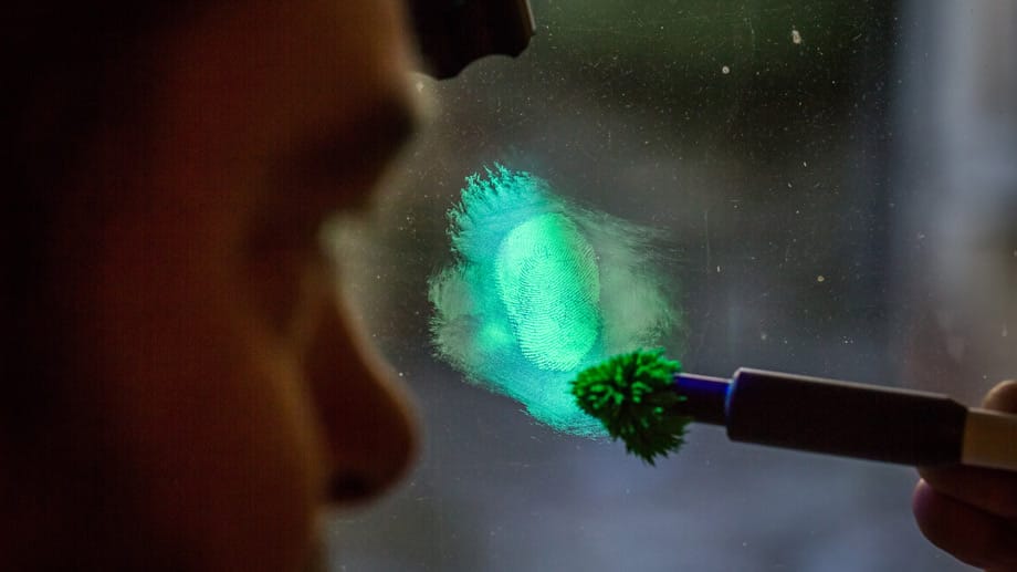 Detektiv Alexander Schrumpf macht mit fluoreszierendem Eisenpulver und einer UV-Taschenlampe einen Fingerabdruck auf einem Fenster sichtbar.