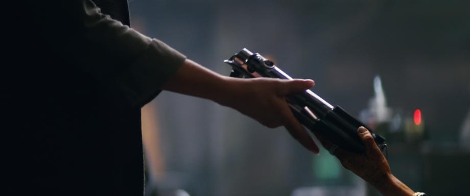 Ein Lichtschwert wird übergeben. Vermutlich handelt es sich bei der Person links um Leia (Carrie Fisher).
