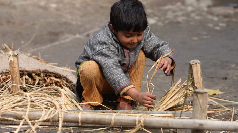 Ein Kind in Kaschmir webt eine traditionelle Matte.
