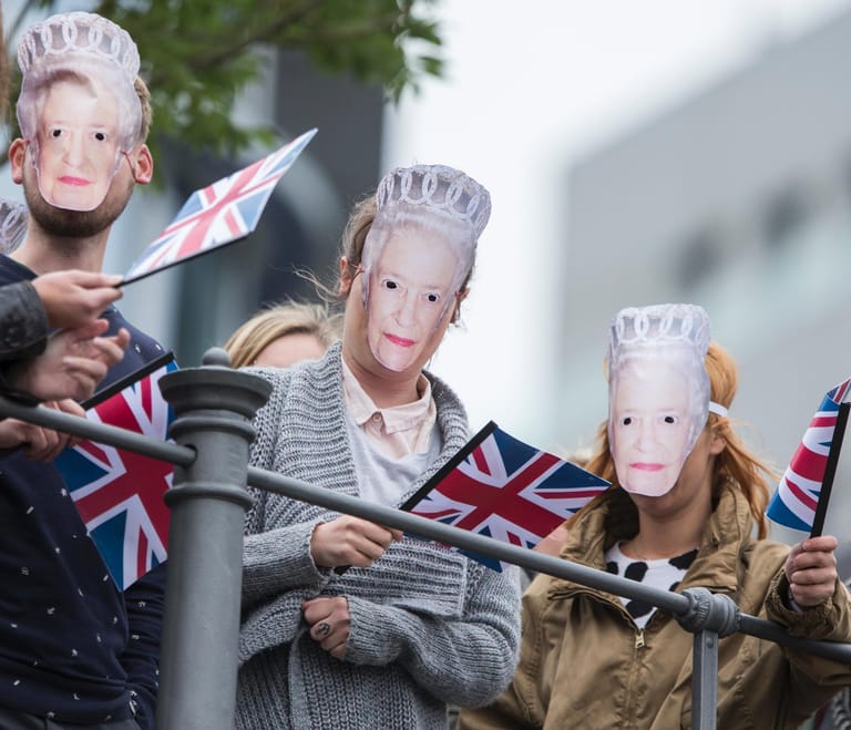 Begeisterte Monarchie-Fans in Berlin: Auf einer Spree-Brücke tragen Zuschauer Masken mit dem Bild der Queen, während die britische Königin eine Bootsfahrt unternimmt.