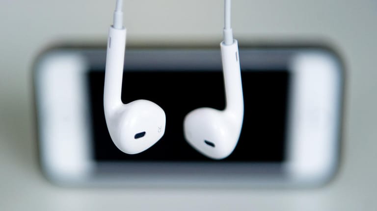 Kopfhörer hängen vor einem Apple iPhone.