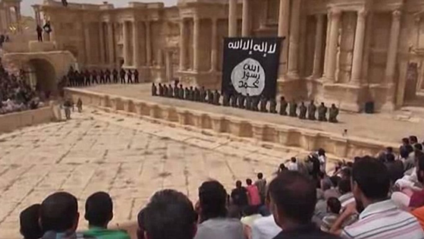 Screenshot aus dem Hinrichtungsvideo aus Palmyra: Die Delinquenten knien vor der übergroßen IS-Flagge.
