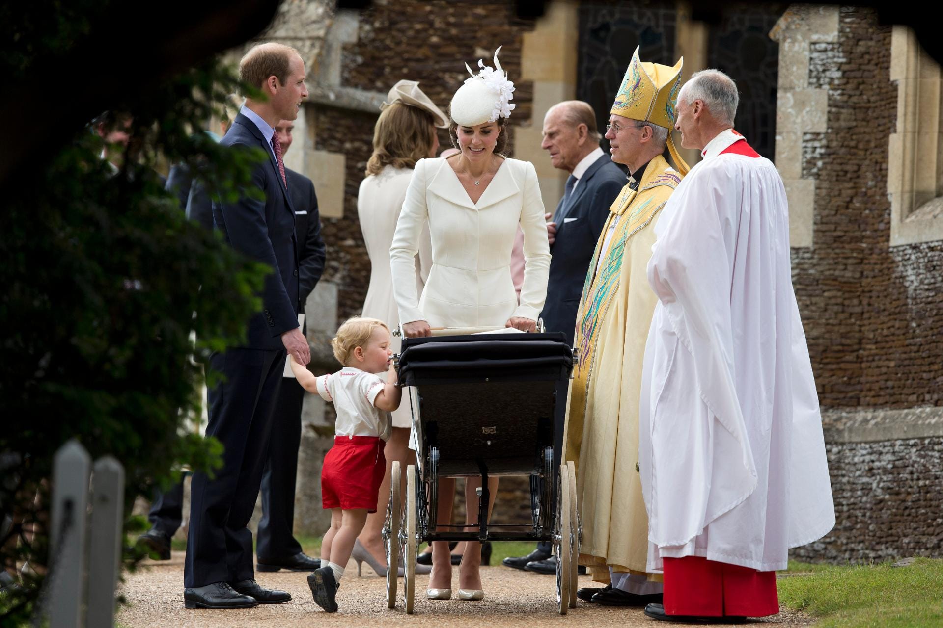 Prinz William, Herzogin Kate und der Erzbischof (2.v.r.) stehen um den Kinderwagen der kleinen Charlotte. Ihr Bruder George vergewissert sich noch einmal, ob alles in Ordnung ist.