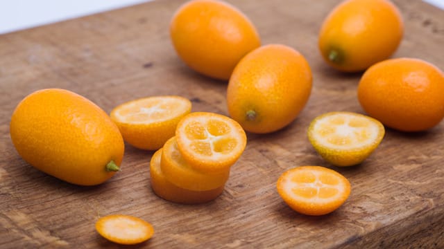 Kumquats von außen und aufgeschnitten auf einem Schneidebrett.