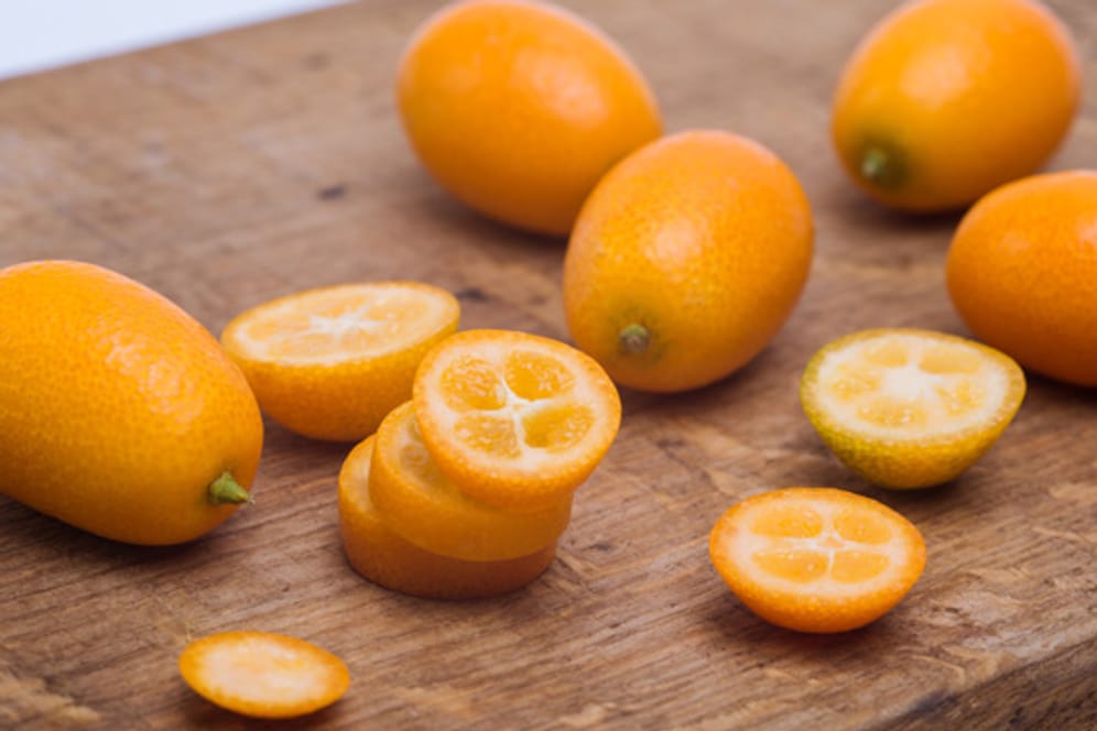 Kumquats von außen und aufgeschnitten auf einem Schneidebrett.