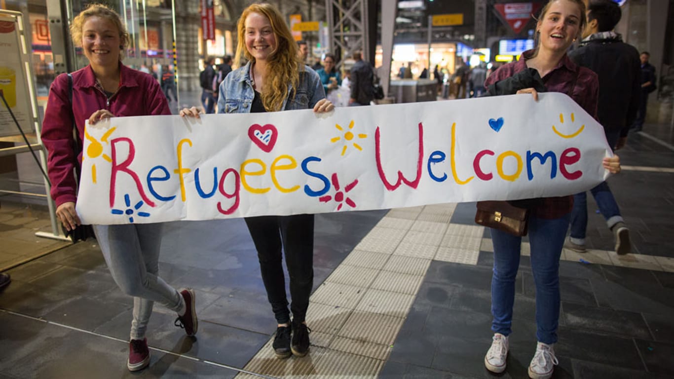 Viele Deutsche heißen die Flüchtlinge willkommen: Hier drei junge Frauen am Frankfurter Hauptbahnhof mit einem Begrüßungsplakat.