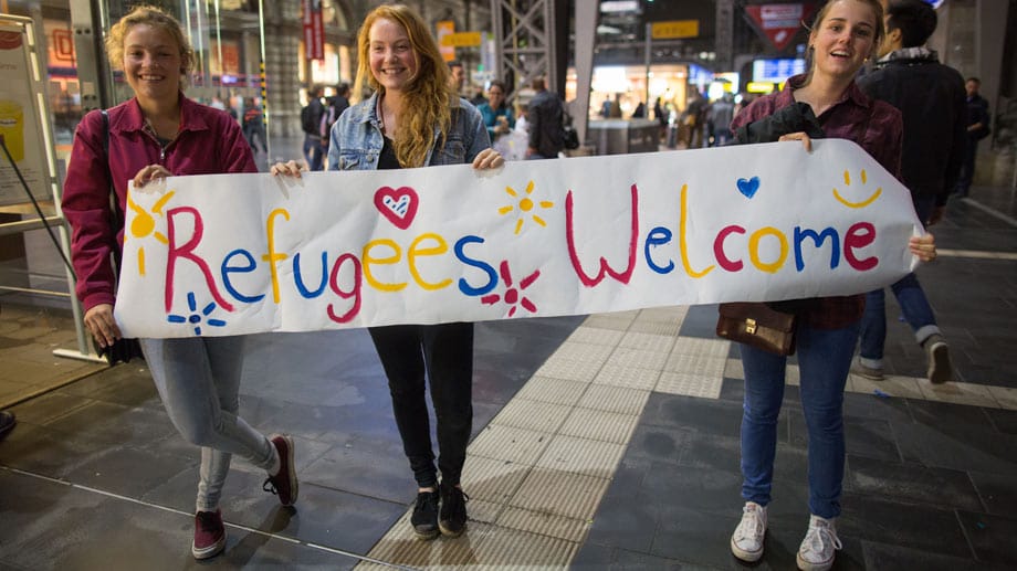 Viele Deutsche heißen die Flüchtlinge willkommen: Hier drei junge Frauen am Frankfurter Hauptbahnhof mit einem Begrüßungsplakat.