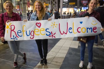 Viele Deutsche heißen die Flüchtlinge willkommen: Hier drei junge Frauen am Frankfurter Hauptbahnhof mit einem Begrüßungsplakat.