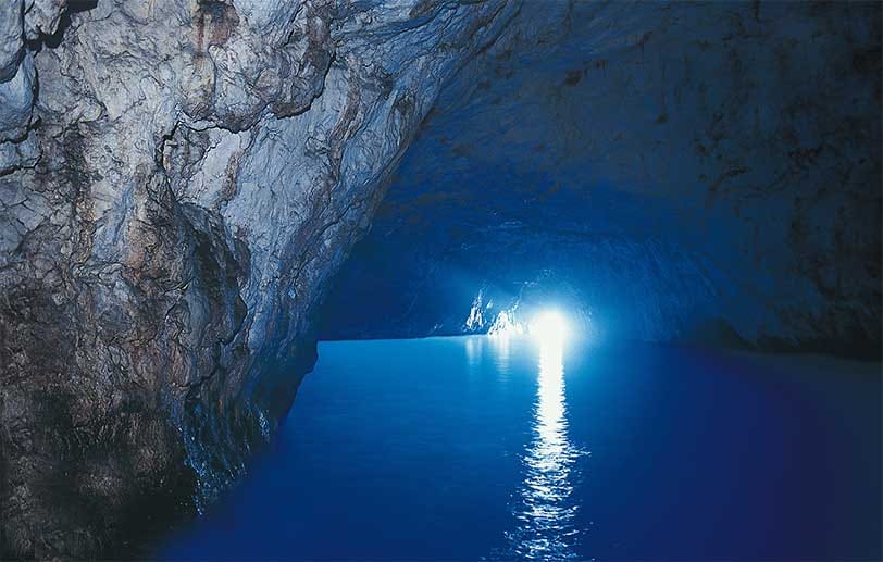 Durch einen kleinen Eingang fällt Licht in die berühmte Blaue Grotte von Capri. Es wird schnell ersichtlich, woher der Name der Meereshöhle kommt.