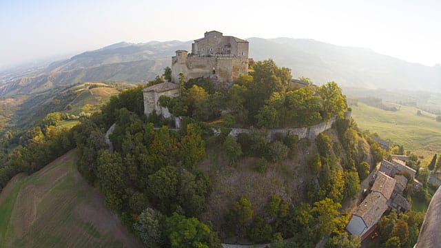 Die Burg Rossena thront über der Landschaft, umgeben von malerischen Hügeln, Gutshöfen und Weinreben.