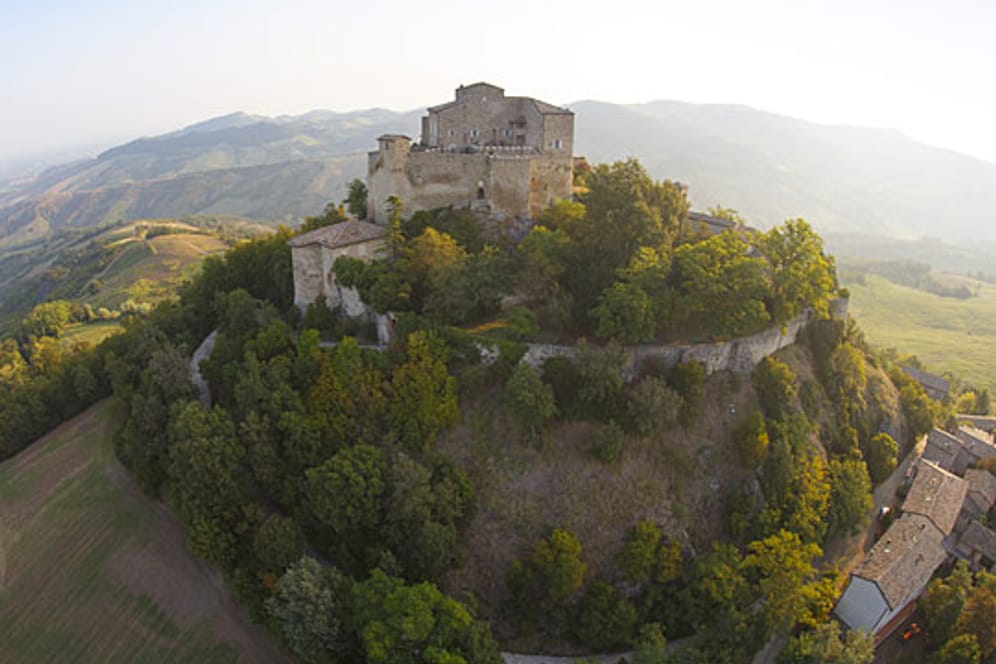 Die Burg Rossena thront über der Landschaft, umgeben von malerischen Hügeln, Gutshöfen und Weinreben.