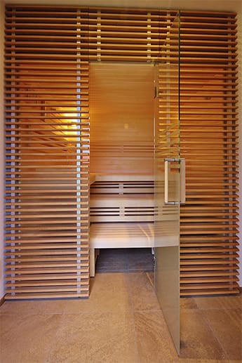 Luftig-transparentes Design für kleinere Räume: Die Glaswand der Sauna ist mit Holzleisten gebrochen.