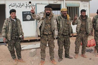 YPG-Kämpfer vor einem eroberten Posten des IS - im Hintergrund das Logo des Islamischen Staates.