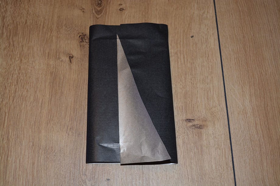 Schlagen Sie das Geschenk nun richtig ein und falten Sie das schräg geschnittene Papier vorne um, so dass eine geometrische Fläche entsteht.