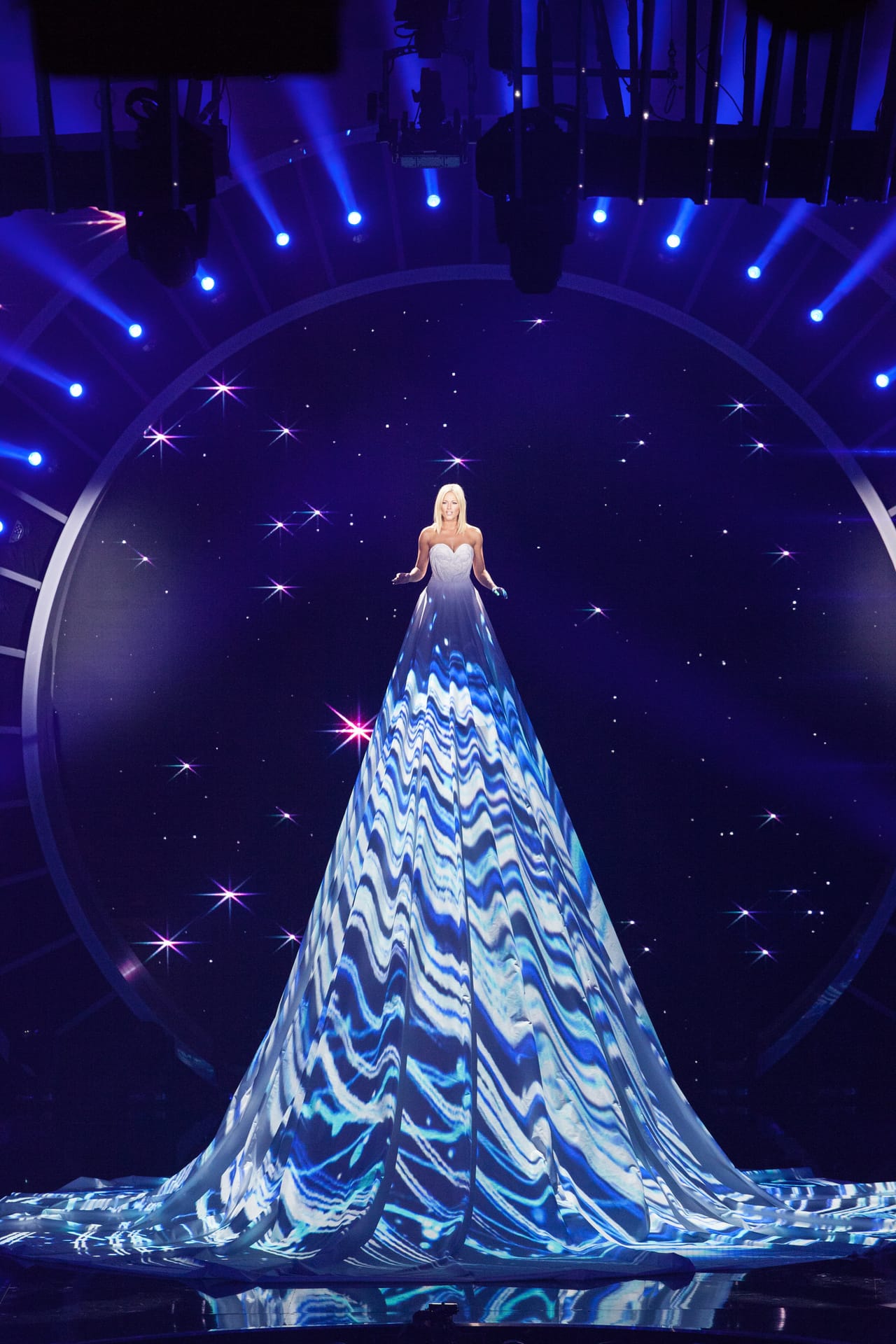 Helene Fischer trägt ein "Riesenkleid", auf dem verschiedene Projektionen abgebildet sind. Sie singt das Lied "Jeden Morgen wird die Sonne neu geboren".