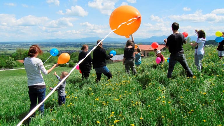 Bei einem Erholungswochenende für trauernde Familien lassen Betroffene und Mitarbeiter der Nicolaidis Youngwings Stiftung auf einer Wiese Luftballons steigen.