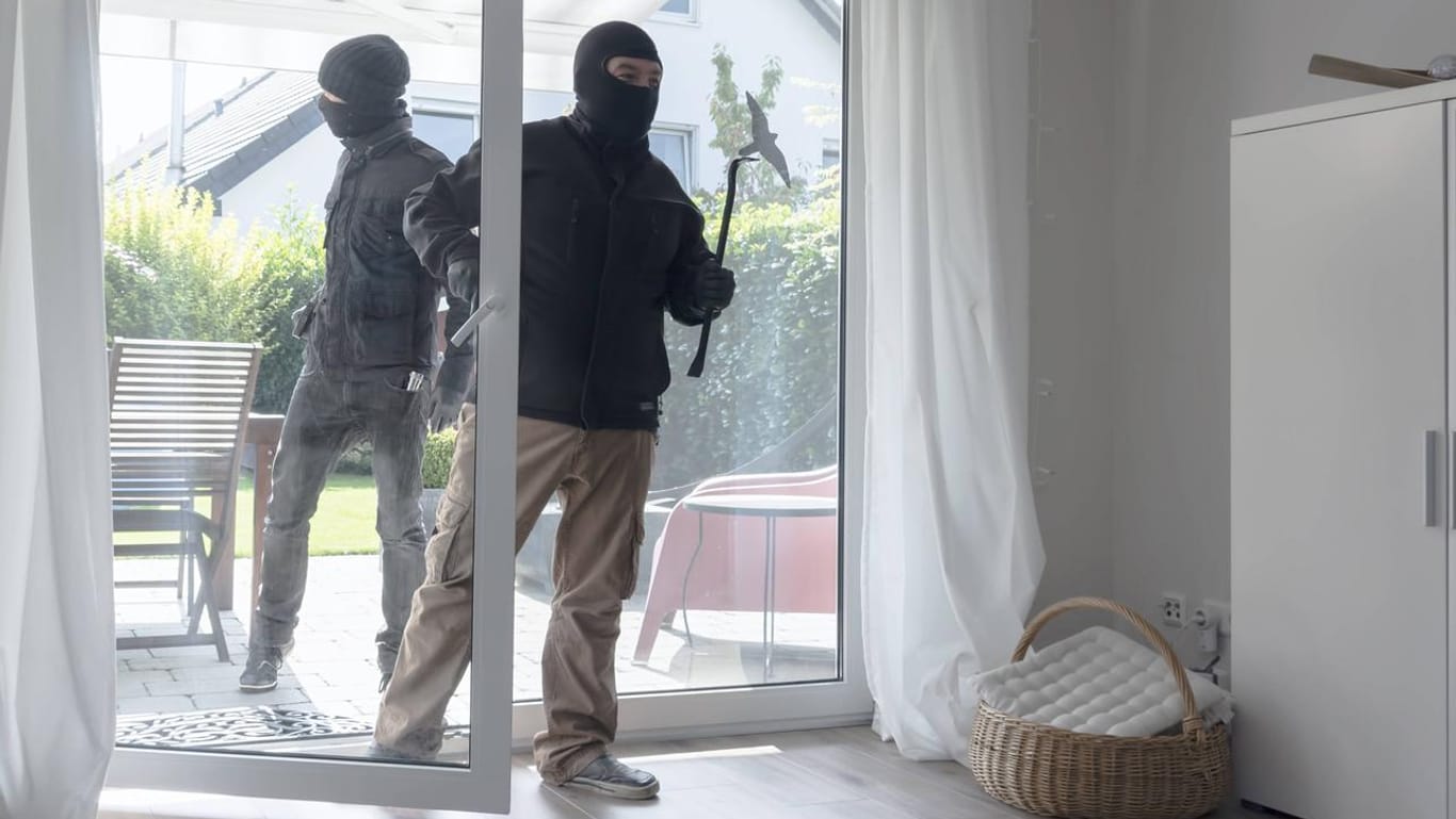 Vermummte Männer öffnen eine Terrassentür: Die Polizei empfiehlt ein defensives Verhalten, wenn Einbrecher im Haus sind.