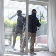 Vermummte Männer öffnen eine Terrassentür: Die Polizei empfiehlt ein defensives Verhalten, wenn Einbrecher im Haus sind.