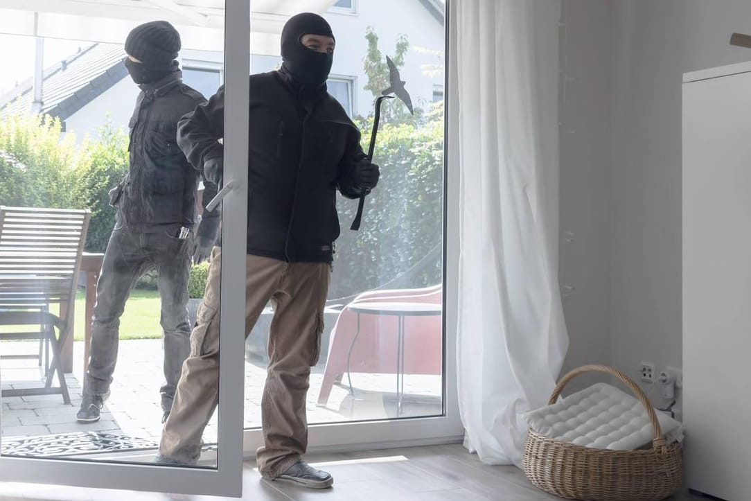 Vermummte Männer öffnen eine Terrassentür: Die Polizei empfiehlt ein defensives Verhalten, wenn Einbrecher im Haus sind.